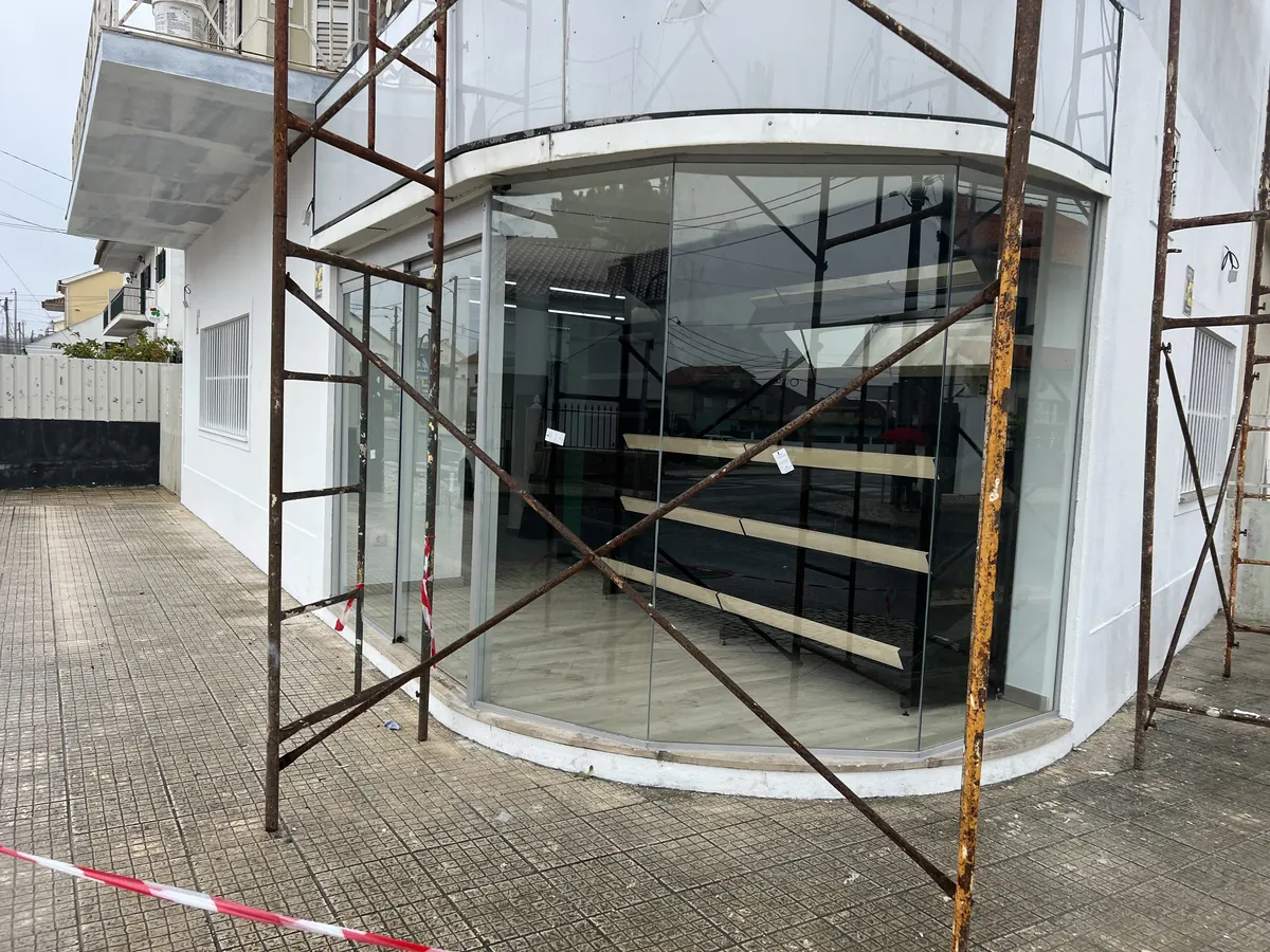 Fachada de vidro curva com porta automática integrada em espaço comercial na Quinta do Conde