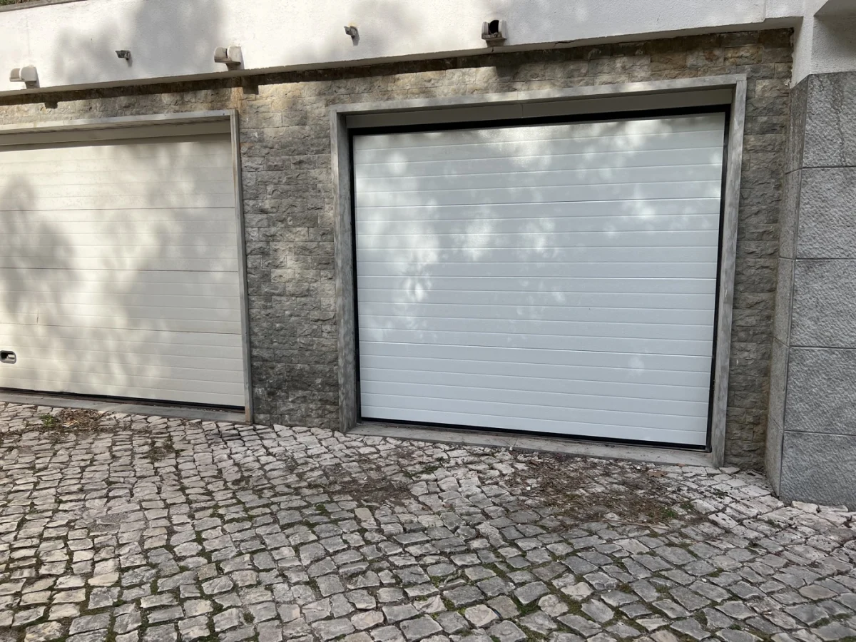 Portão de garagem seccionado branco em fachada de pedra
